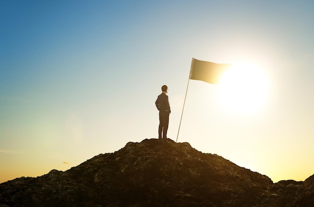 Success and achievement concept silhouette of businessman with flag on mountain top