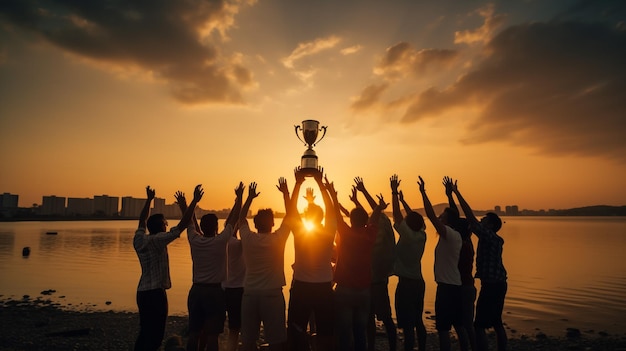 Success of teamwork joint achievement of goal in business and life Winning team is holding trophy in hands Silhouettes of many hands in sunset