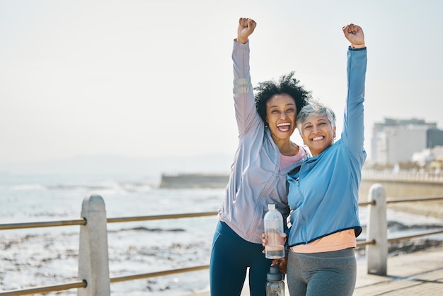 Photo success women and friends fist pump and fitness goals with running outdoor winning and health happy senior female people exercise achievement while training for marathon with cheers at beach