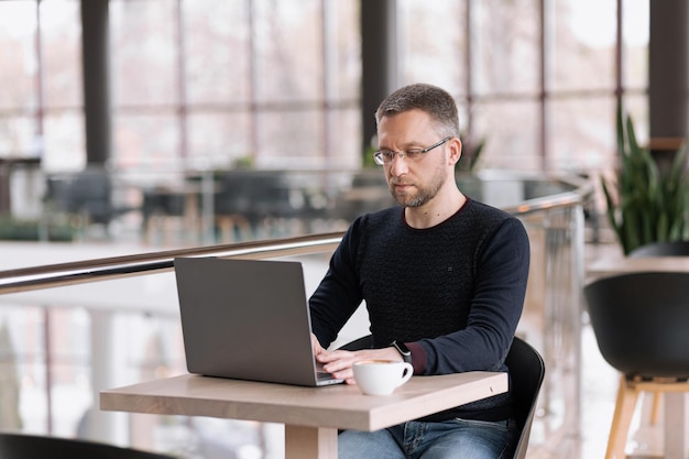 Successful adult man with glasses works on a laptop in a cafe