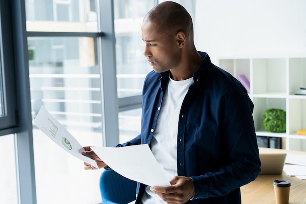 Imprenditore africano di successo che studia documenti con sguardo attento e concentrato, bevendo caffè al bar. uomo d'affari dalla pelle scura concentrato su questioni di lavoro, firmando documenti per affari