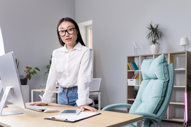 Successful asian business woman at workplace in office looking at camera portrait of strong leader