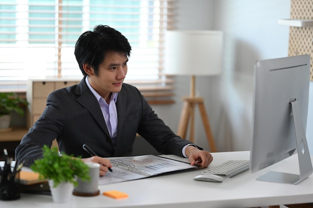 세련된 사무실에서 일하는 검은 양복을 입은 성공적인 아시아 사업가