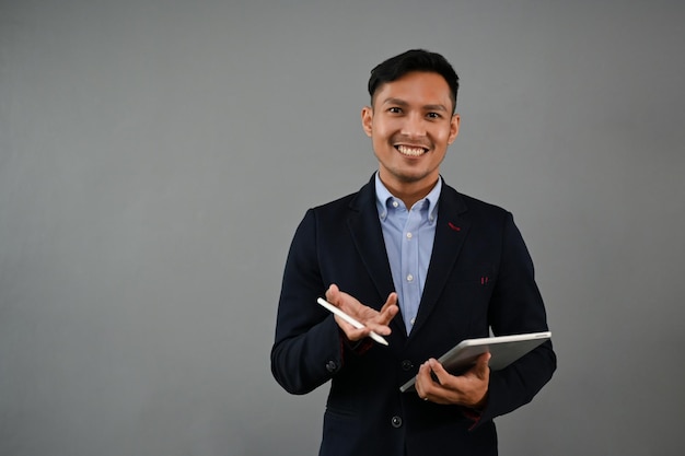 Successful Asian businessman stands on an isolated gray background with his tablet