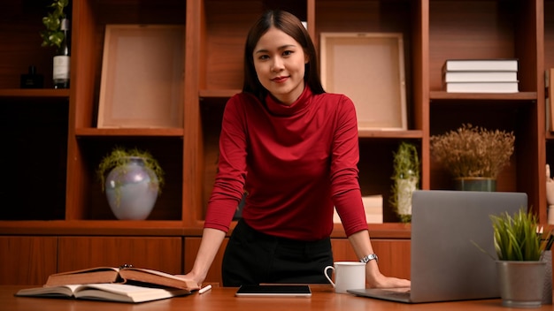 Successful Asian businesswoman or female executive manager standing leaned at her office desk