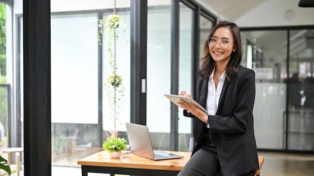 Successful Asian businesswoman leaning on table holding a digital tablet