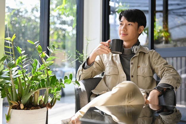 Успешный азиатский мужчина наслаждается утренним кофе в кофейне, мечтая