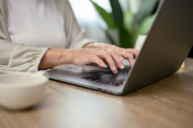 Successful Asianaged woman typing on keyboard using laptop computer cropped