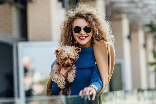 Successful attractive woman wearing at nude coat holding Yorkshire terrier.