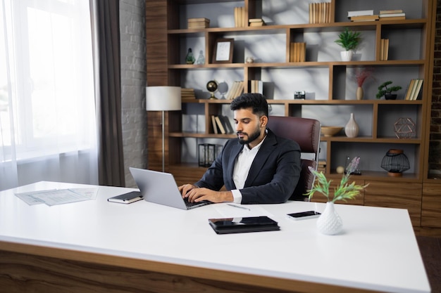 Successful bearded businessman in stylish uit working on laptop computer on modern office