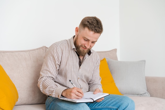 Successful bearded young man writes notes in notebook while sitting at home