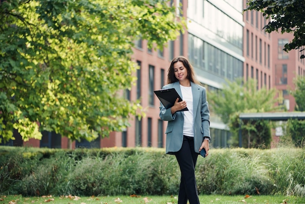 Successful beautiful business woman in suit with document walking to the meeting near modern office