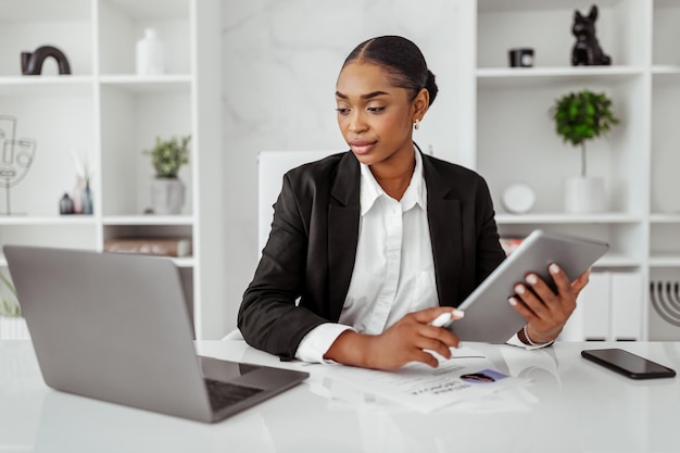 Photo successful black businesswoman using digital tablet and laptop browsing business app or responding