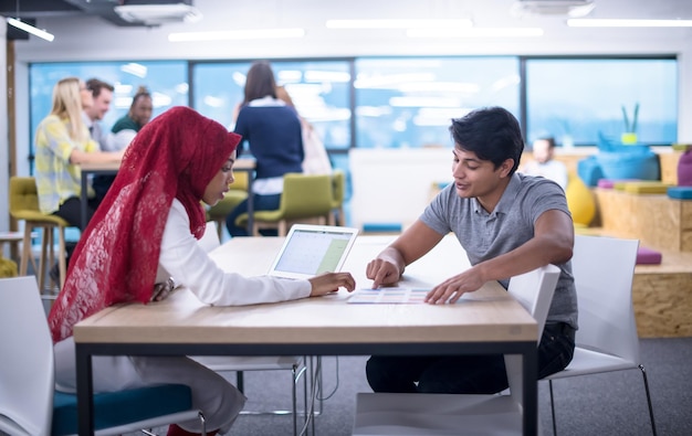 successful black muslim business woman having a meeting with her indian male colleague working on the laptop at modern startup office