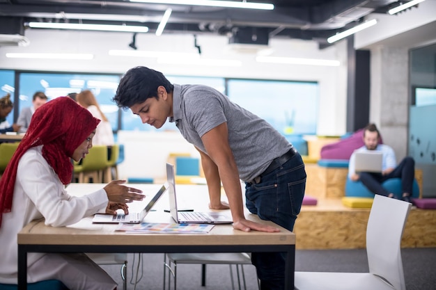 successful black muslim business woman having a meeting with her indian male colleague working on the laptop at modern startup office