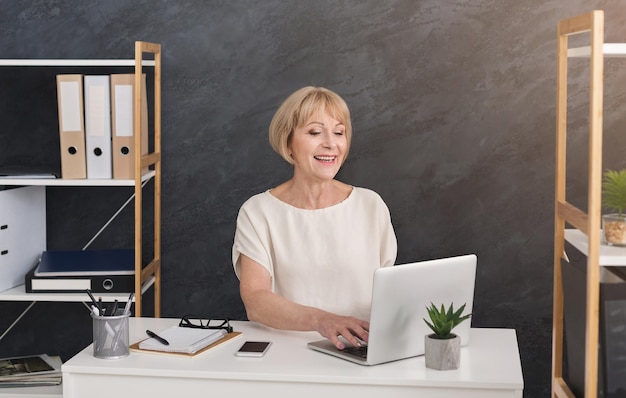 Successful blond mature businesswoman in office. Boss working on laptop at workplace