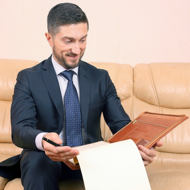 Successful business man engaged in business documents sitting on a leather sofa