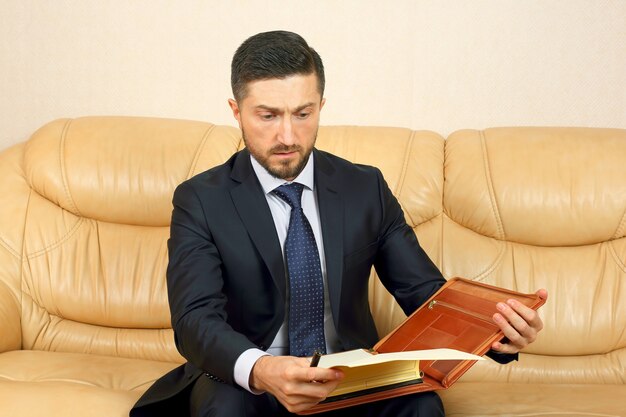 Successful business man engaged in business documents sitting on a leather sofa
