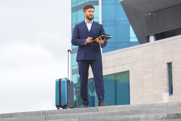 Successful business man stands on the steps at office building with a project business documents in his hands