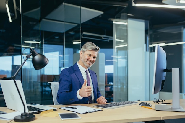 Successful business manager businessman working in modern office looking at camera smiling and holding thumbs up