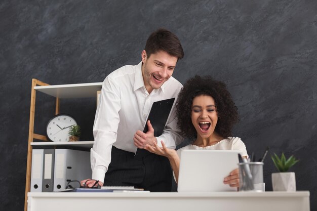 Successful business partners happy, celebrating successful project, looking at laptop. Happy colleagues raising their arms, copy space