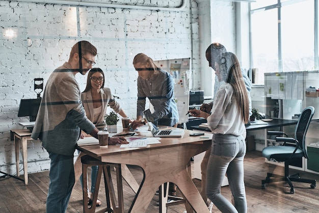 Successful business team. Group of young modern people in smart casual wear discussing business while standing behind the glass wall in the creative office