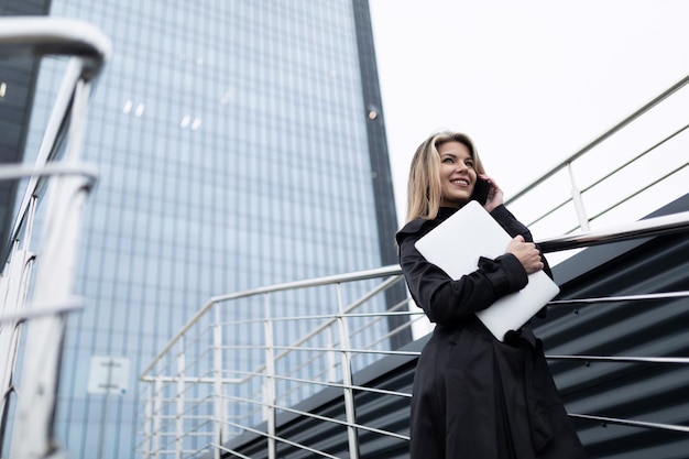 Donna d'affari di successo sullo sfondo di un moderno edificio per uffici con un laptop e un cellulare