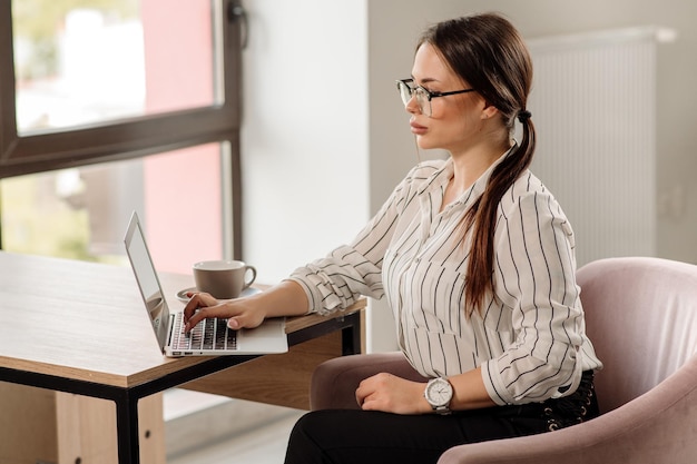 Successful business woman in shirt wearing glasses working with a laptop in the office