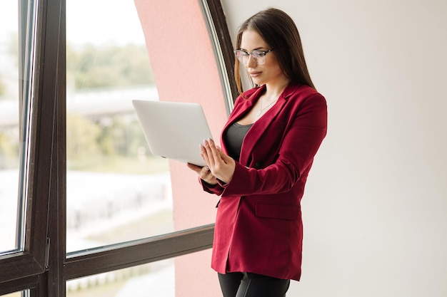 Successful business woman well dressed holding laptop and posing in the office room