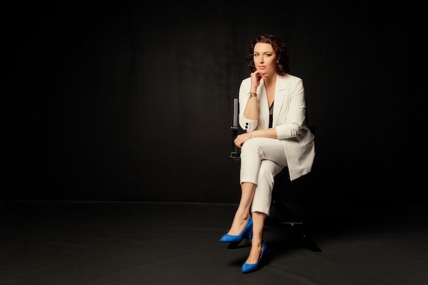 Успешная деловая женщина в белом пиджаке сидит на стуле
