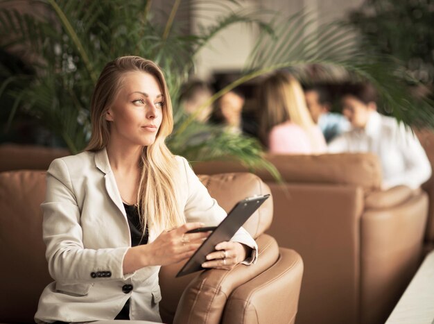 Successful business woman with documents sitting in a chair in a lobby of a modern office