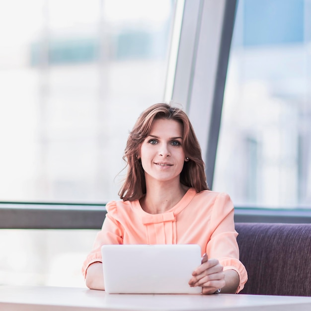 Успешная деловая женщина с планшетом сидит за столом в холле офиса