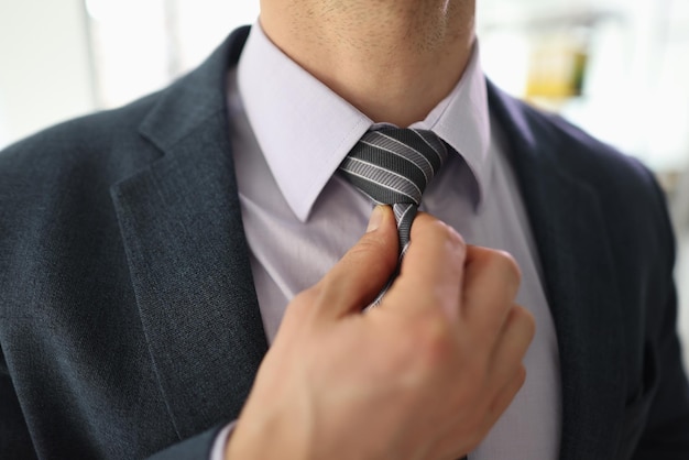 Successful businessman adjusts striped tie with hand to feel comfortable young man in classic