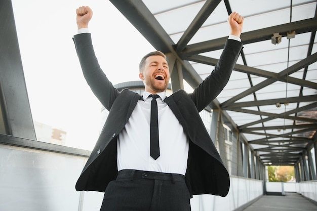 Successful businessman celebrating his victory with arms up on cityscape background