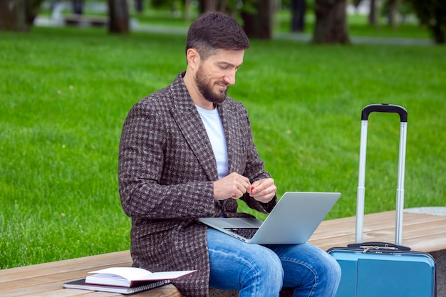 Успешный бизнесмен сидит на городской скамейке и занимается бизнесом с документами и ноутбуком