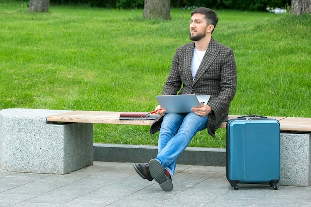 Успешный бизнесмен сидит на городской скамейке и занимается бизнесом с документами и ноутбуком