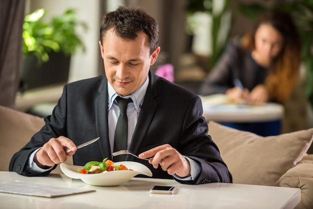 Successful businessman sitting in cafe and eating salad