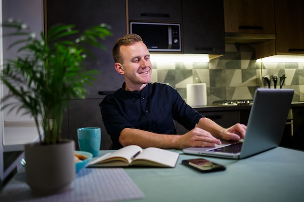 Successful businessman sitting at home at the table, looks at the laptop screen, feels pride in the work done, serene man works, work at home