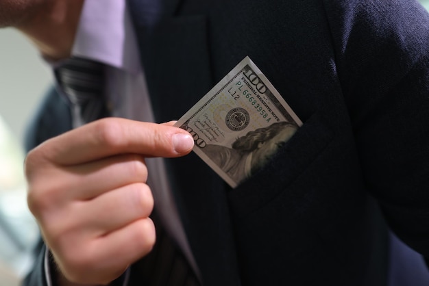 Successful businessman takes dollar banknote out of jacket chest pocket man in classic suit