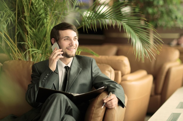 Успешный бизнесмен с деловыми бумагами разговаривает по смартфону сидя