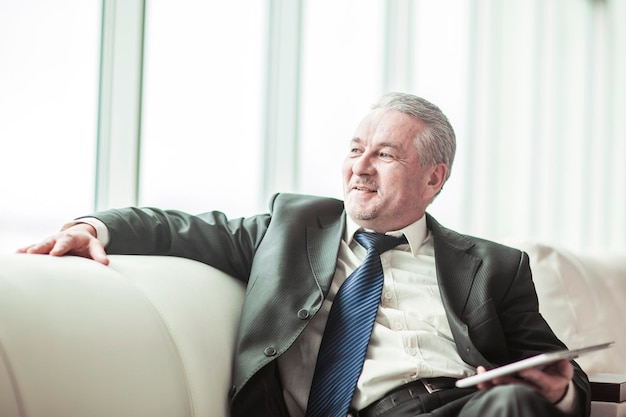 Successful businessman with digital tablet sitting on the sofa in the private office