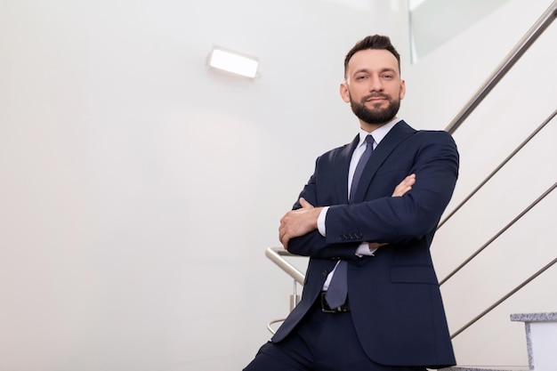 A successful businessman with his arms crossed on his chest stands on the stairs leading up