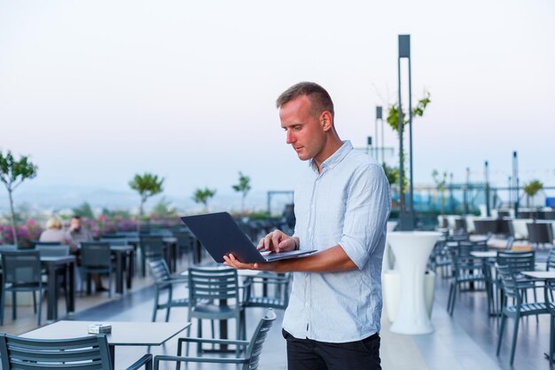 A successful businessman works on a laptop on a hotel terrace and finds time to remotely manage employees while on holiday at an exotic resort Man in shorts and shirt