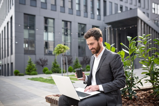 Successful businesswoman drinking hot drink sitting on bench and working on laptop, successful freelancer man