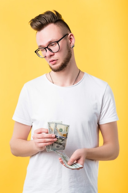 Successful career. Portrait of smart, successful millennial guy. Young man in glasses holding 100 dollar bills, calculating his salary.