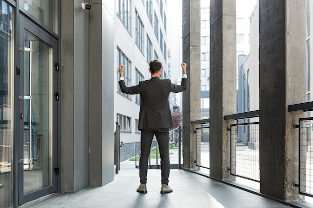 Foto riuscito uomo d'affari caucasico con le braccia alzate per celebrare la vittoria. concetto: successo, crescita di carriera, vittoria, libertà. silhouette uomo d'affari dipendente sullo sfondo di un moderno edificio per uffici. al di fuori