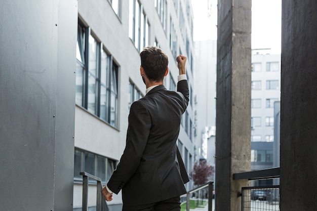 Foto riuscito uomo d'affari caucasico con le braccia alzate per celebrare la vittoria. concetto: successo, crescita di carriera, vittoria, libertà. silhouette uomo d'affari dipendente sullo sfondo di un moderno edificio per uffici. al di fuori