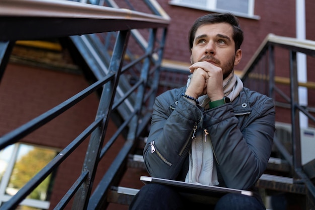 Successful caucasian man sits thoughtfully on the stairs in the street