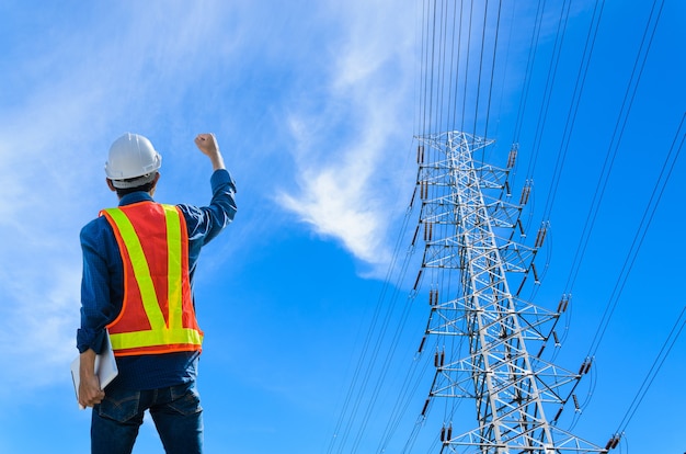 成功したエンジニアは、青い背景の高電圧ポールに立ち向かいます。