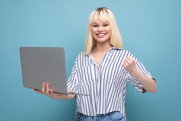 Successful freelance blonde young woman in striped shirt with laptop on studio background